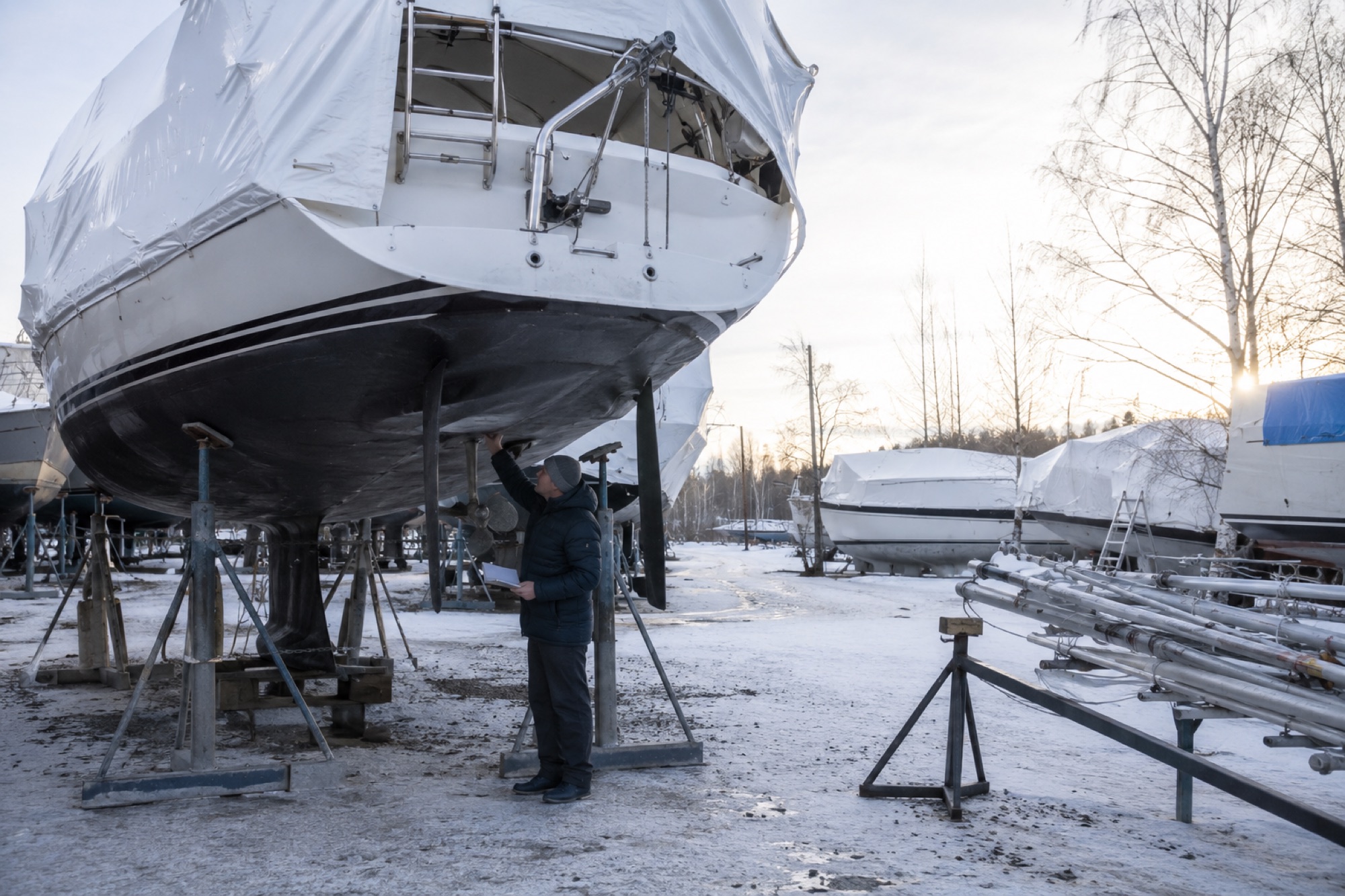 Sailboat on cradle in winter boatyard with snow on ground, owner inspecting